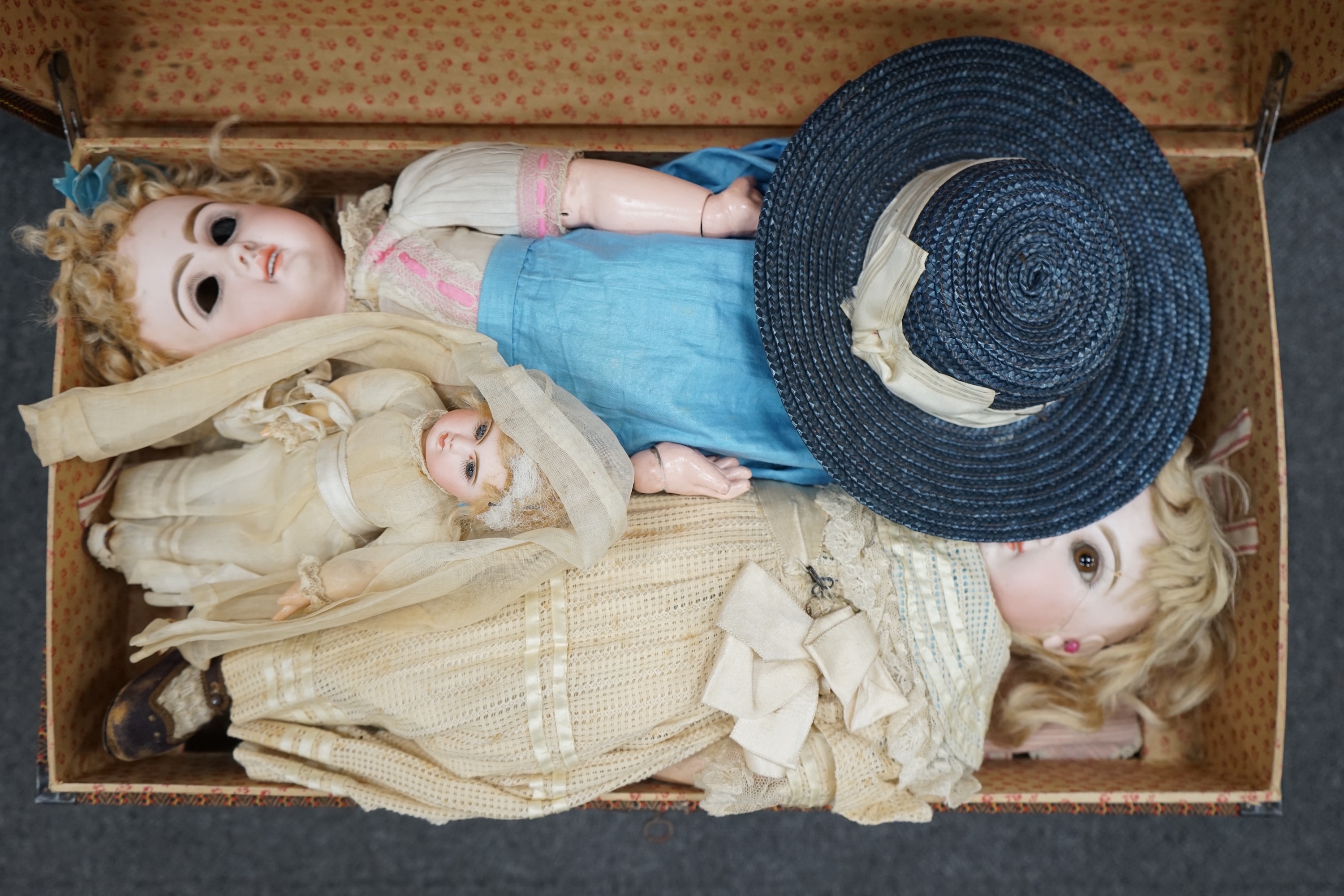 A Tête Jumeau bisque doll, closed mouth and paperweight eyes, jointed wood and composition body, two other French bisque dolls and assorted clothing, all contained within a three-layer wood and metal-bound cabin trunk, J